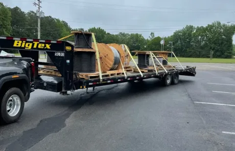 Hauling Industrial Supplies Pickup truck towing a flatbed trailer loaded with industrial pipes and a large wooden spool.