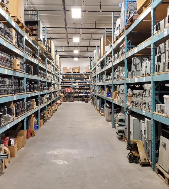 electrical_surplus_items_we_handle_1x Aisle view of a large warehouse with tall shelving units filled with various industrial parts and equipment, showcasing the extensive inventory available at United Industries.