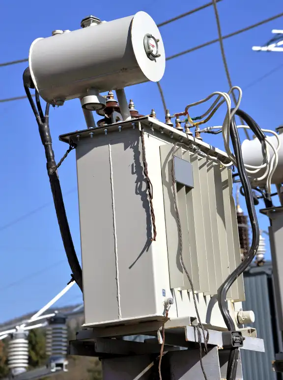 Used Electrical Transformer for Sale Large outdoor electrical transformer with cooling fins and high-voltage bushings against a bright blue sky.